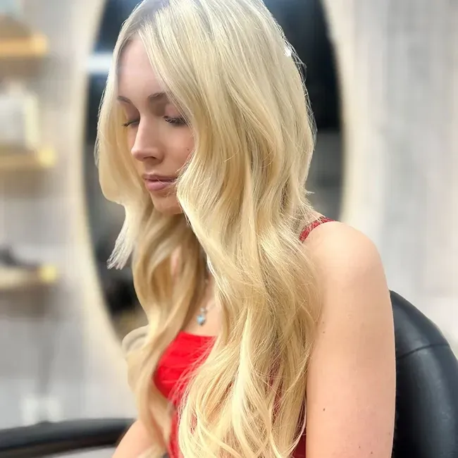 Blonde woman in a red top seated indoors, looking down thoughtfully