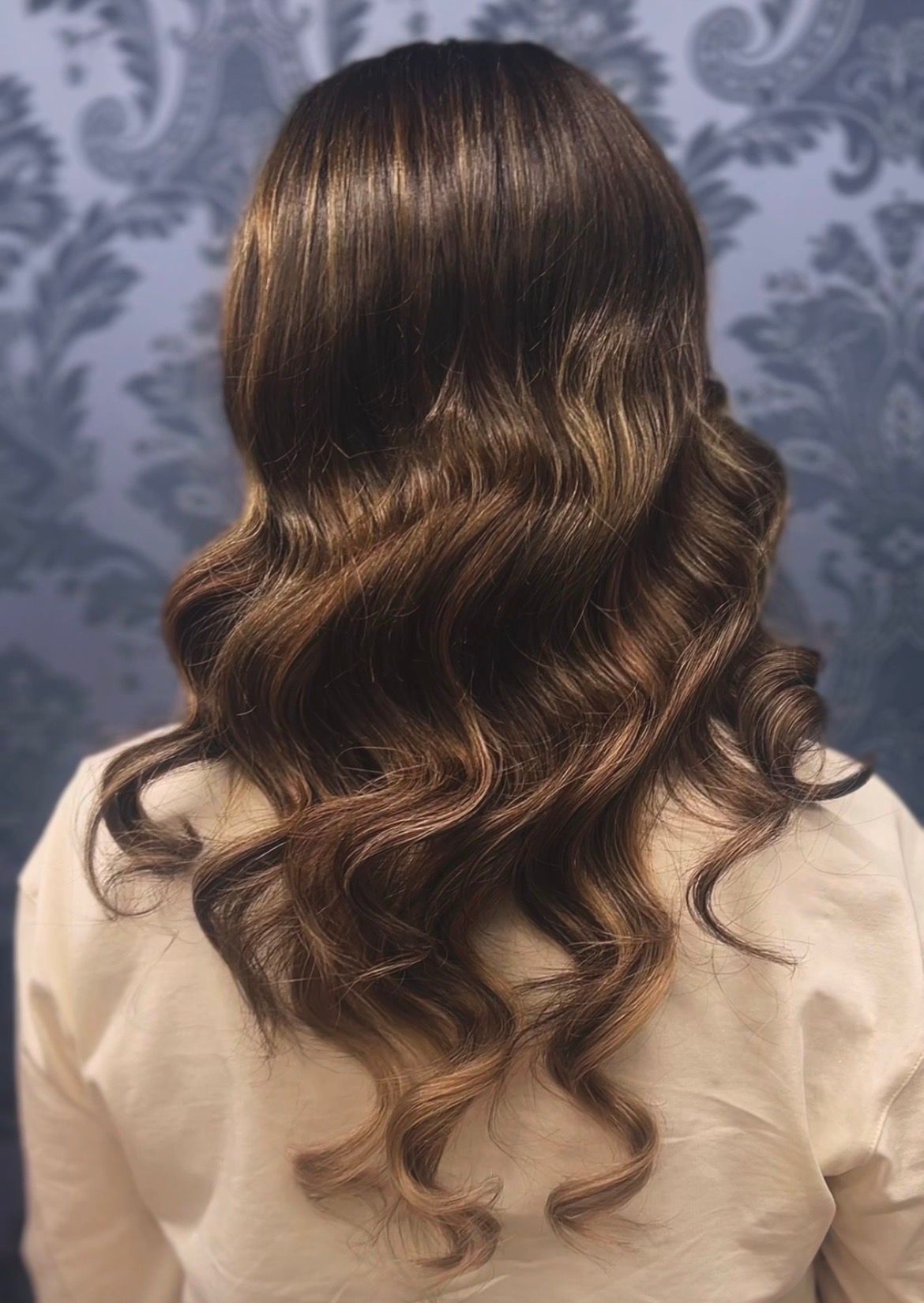 Back view of long wavy brown hair with soft curls against a patterned background