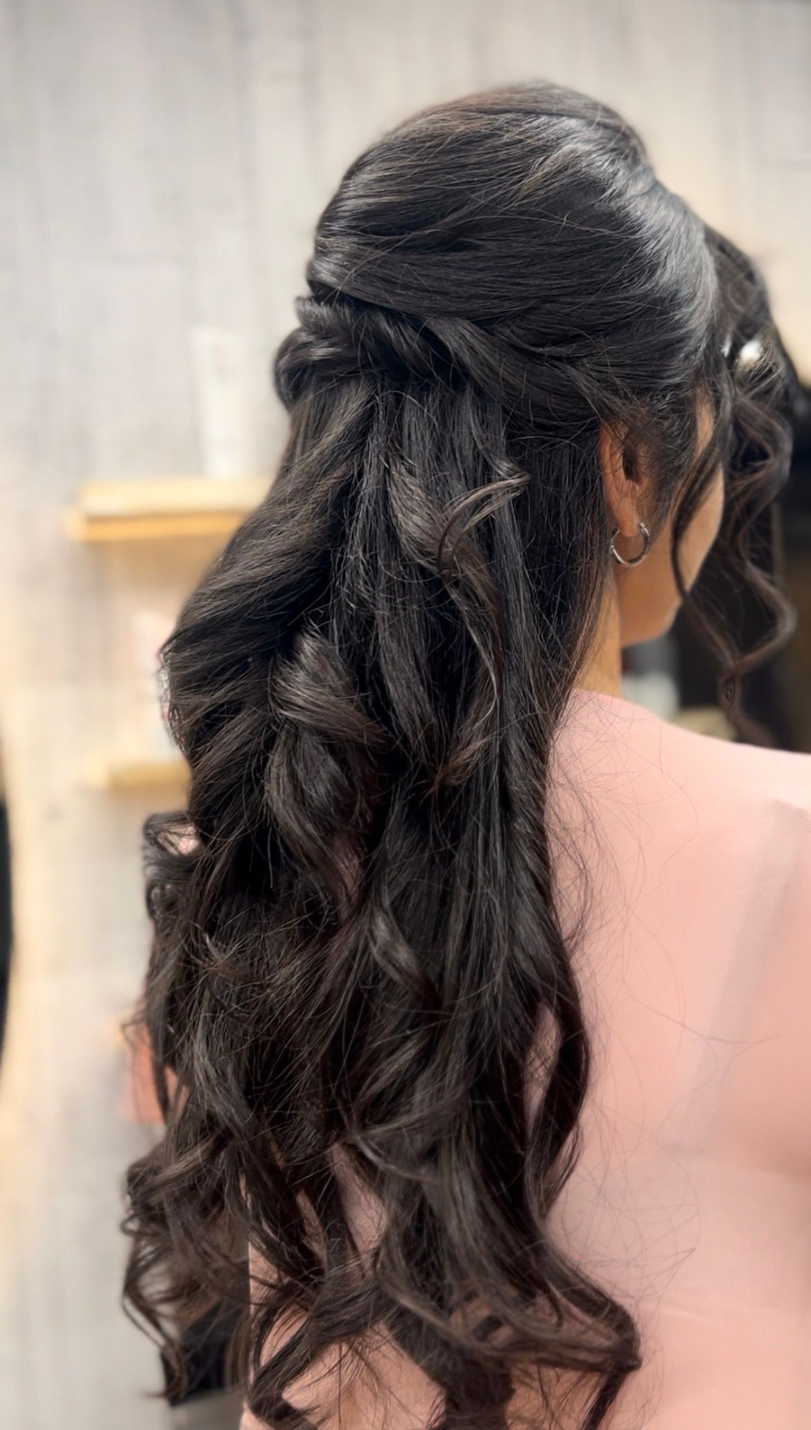 Long dark wavy half-up hairstyle with loose curls, shown from the back against a light indoor background