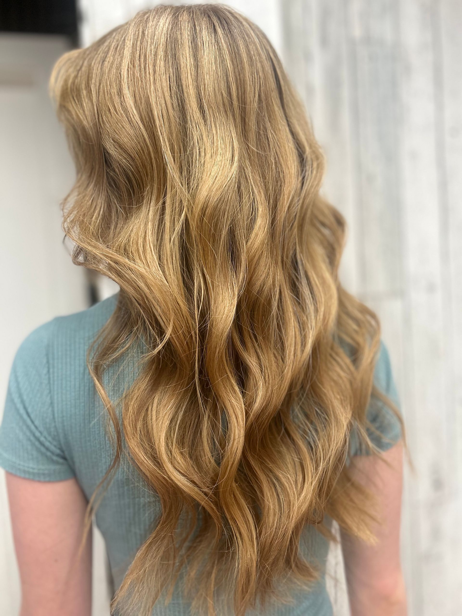 Long wavy blonde hair with subtle highlights cascading down the back, against a light background