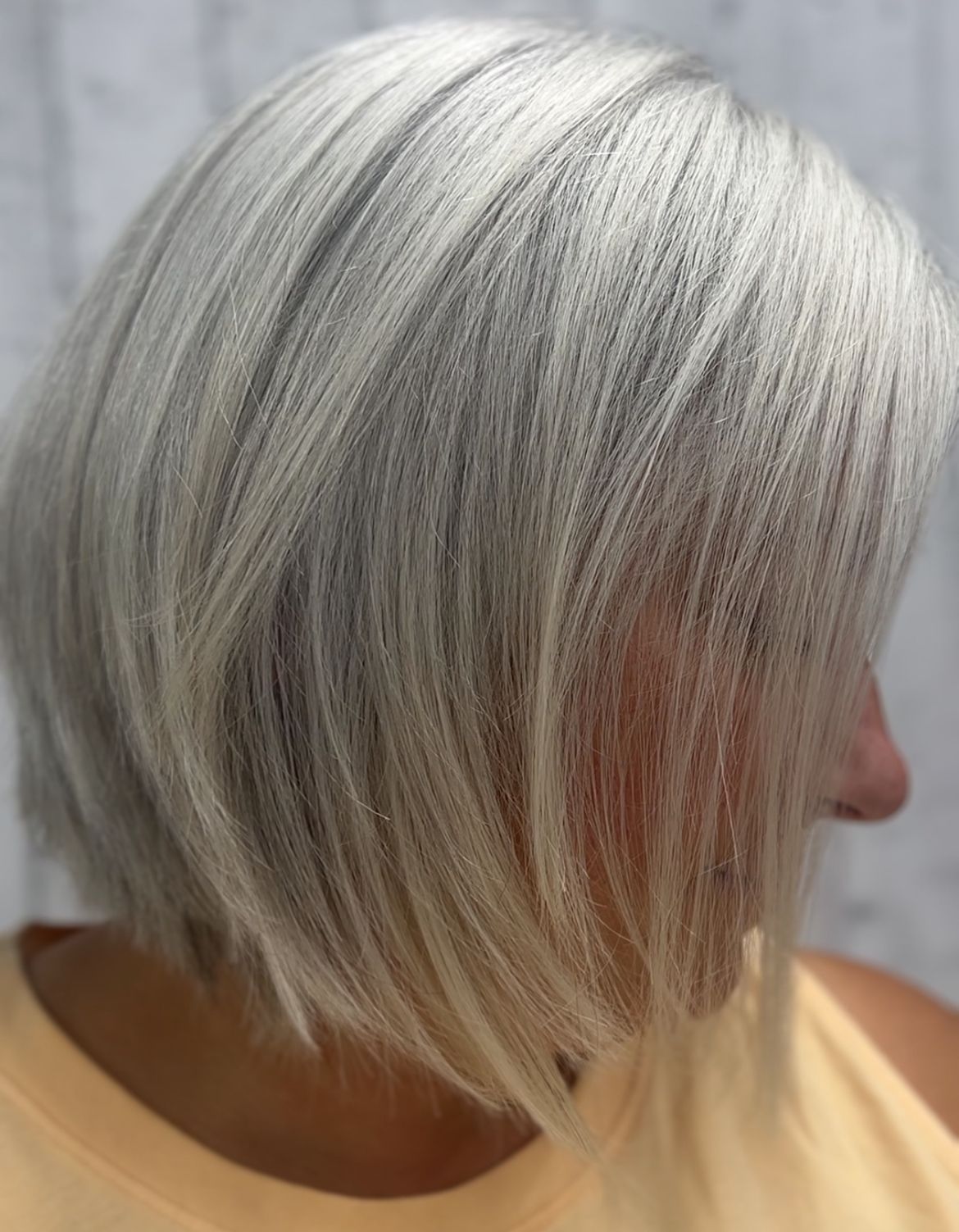 Side profile of a person with a short silver-blonde bob haircut against a gray background