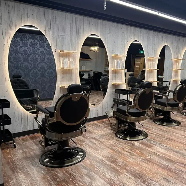 Modern barbershop with black chairs, oval mirrors, patterned wallpaper, and wood flooring