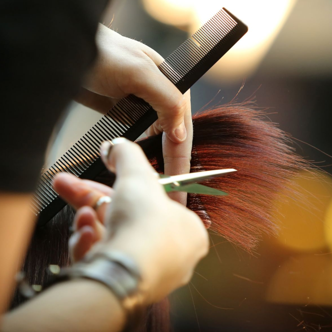 Hairdresser cutting reddish hair with scissors and comb in a salon close-up