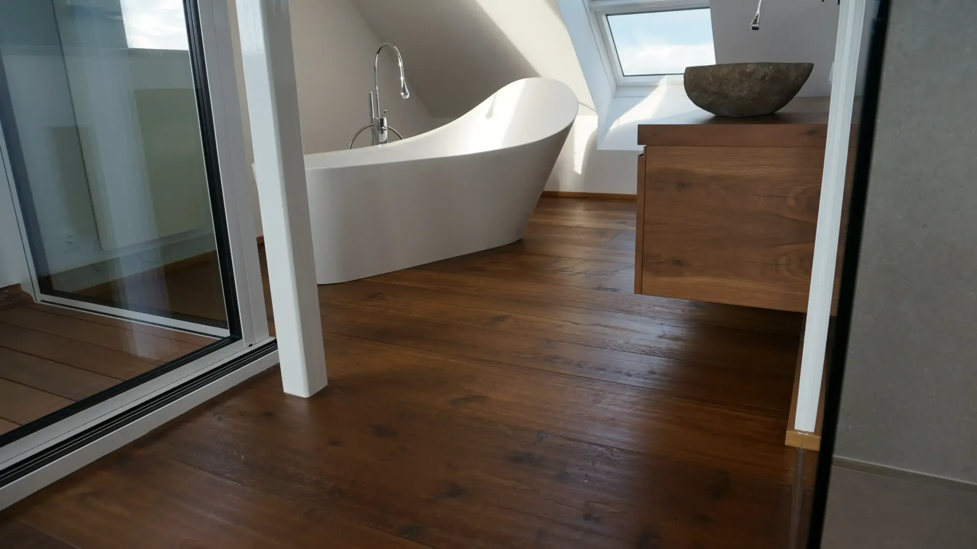 Badezimmer mit Holzboden, weißer Badewanne, Holzwaschtisch und kleinen Fenstern.