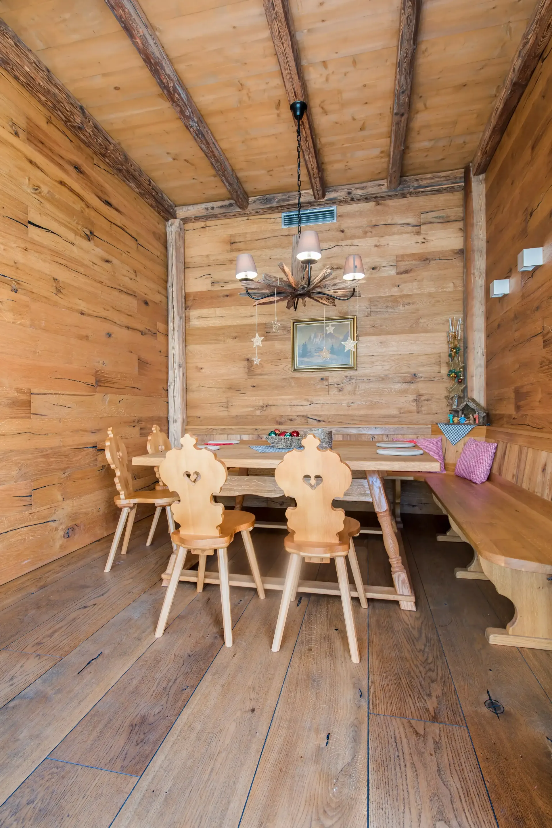 Esszimmer aus Holz mit Tisch, Stühlen, Bank, Kronleuchter und holzgetäfelten Wänden und Decke.