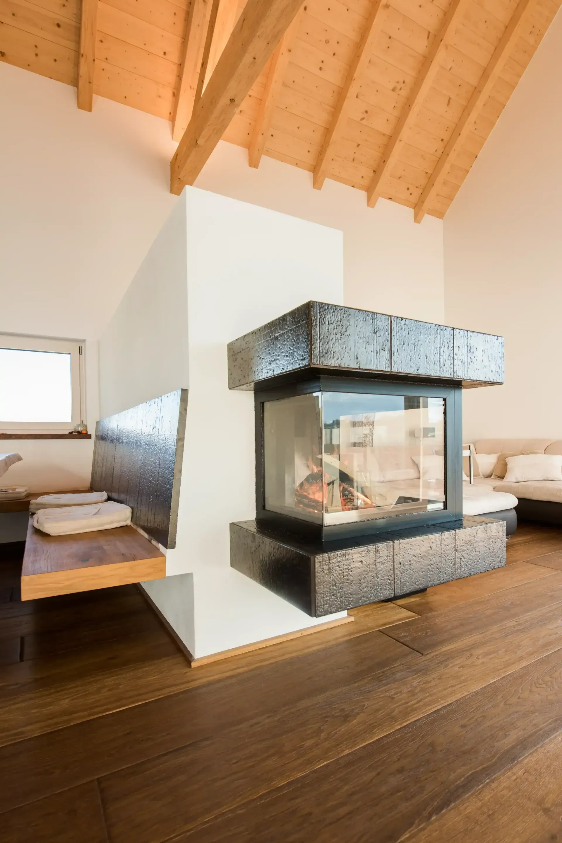 Modernes Wohnzimmer mit Kamin. Dunkler Holzboden, Holzbalkendecke, weiße Wände, Steinkamin.