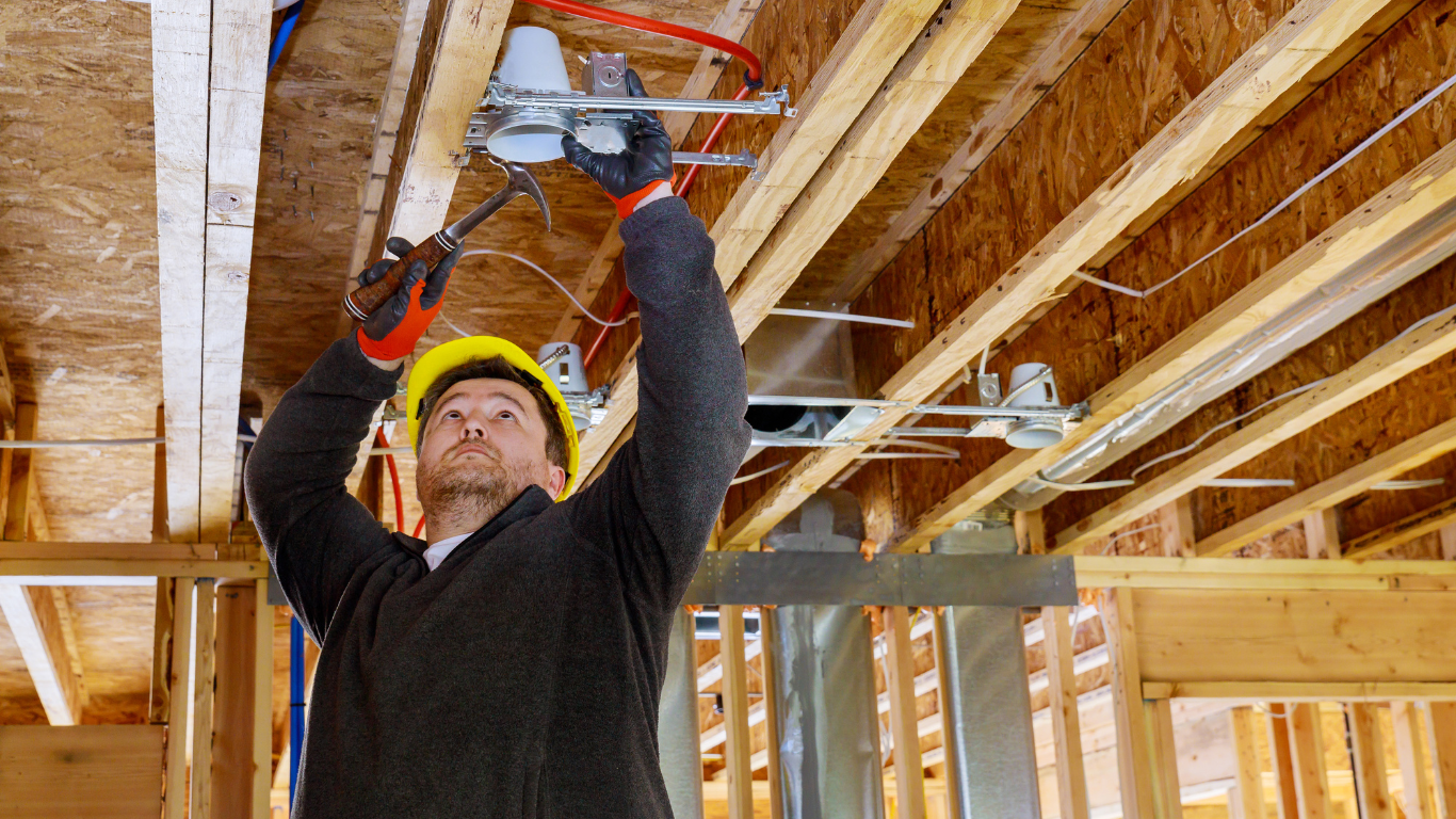 An electrical contractor is working on the ceiling of a house under construction.