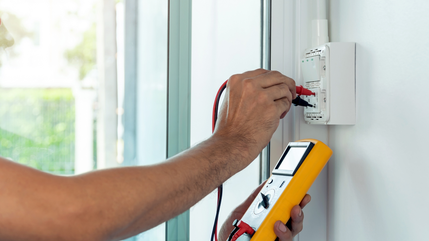A man is using a multimeter to test an electrical outlet.