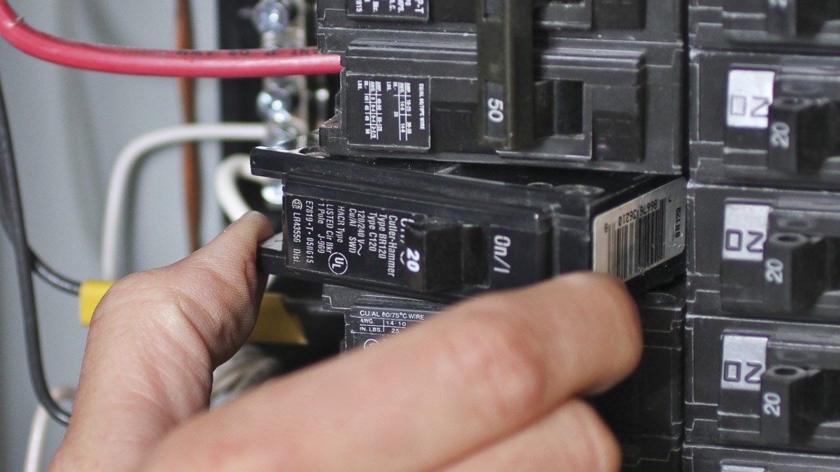 A person is holding a breaker in a electrical box.