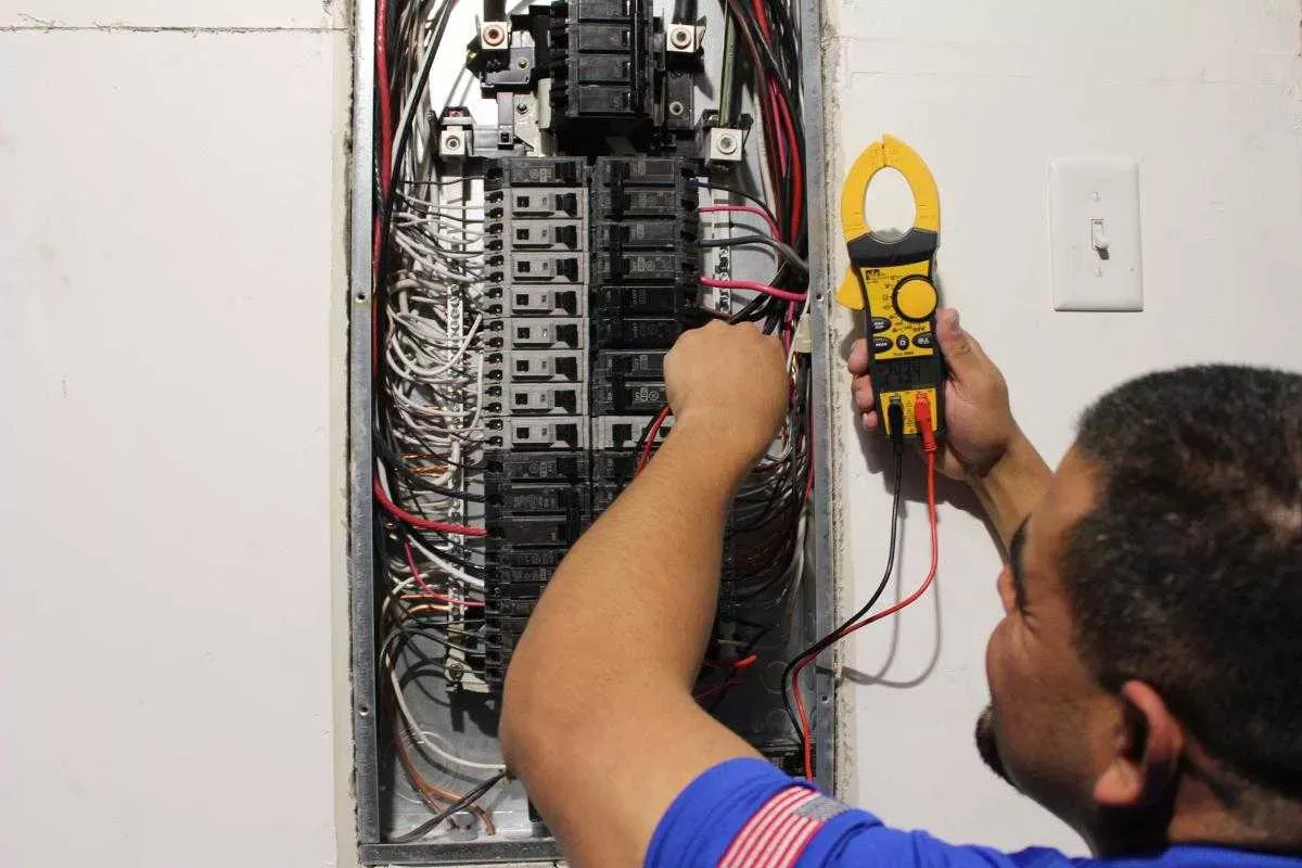A man is working on an electrical panel with a clamp meter.