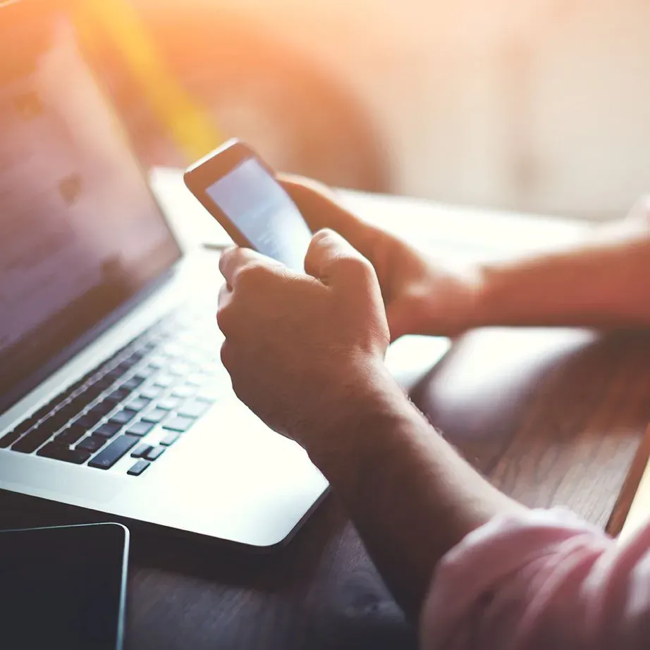 A person holding a cell phone in front of a laptop