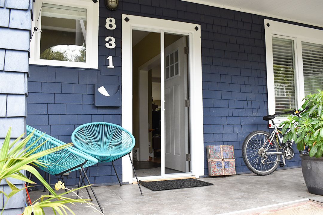 Blue house porch with open front door, teal chair, bicycle, and potted plants