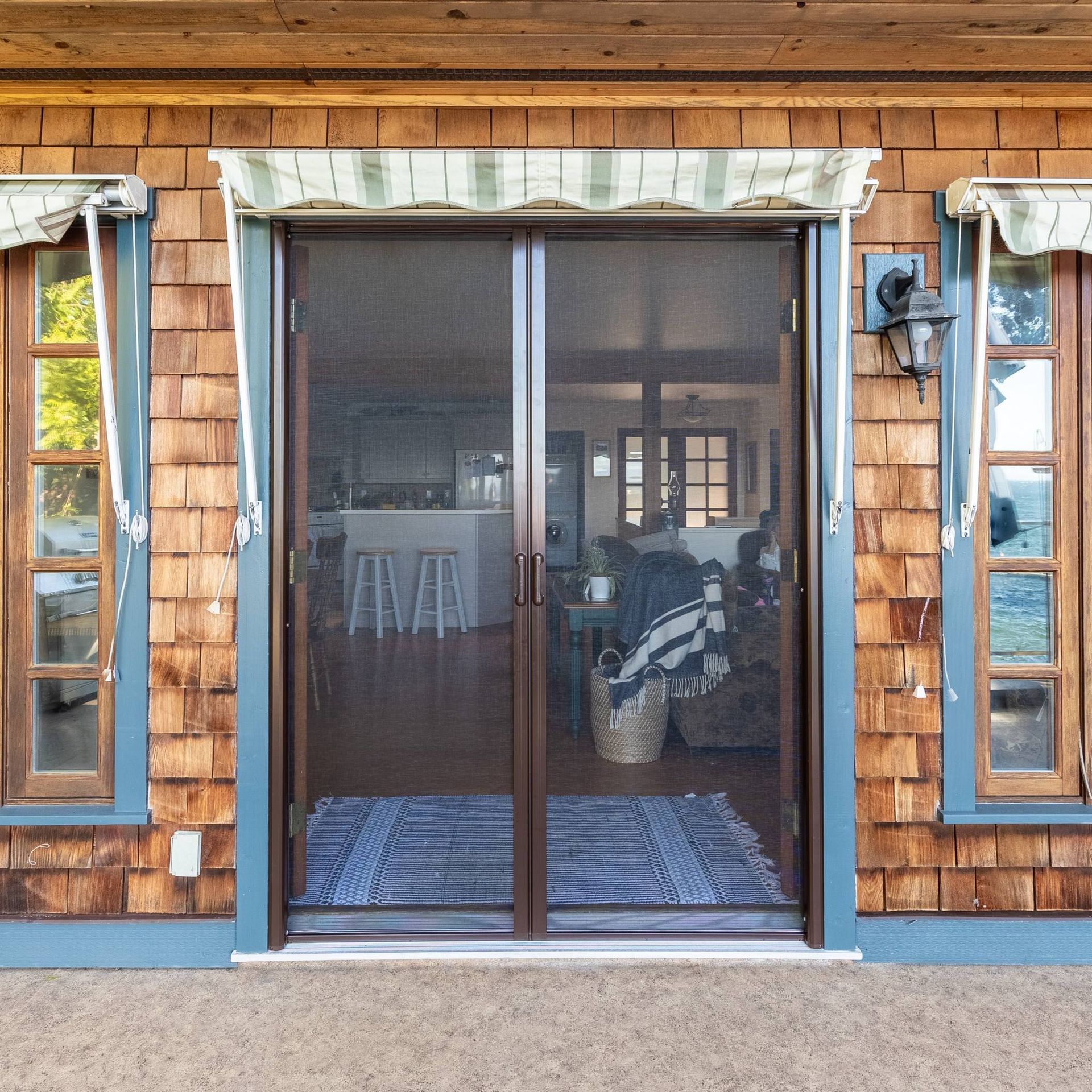 Front view of a screened porch door on a shingled house, flanked by narrow windows.