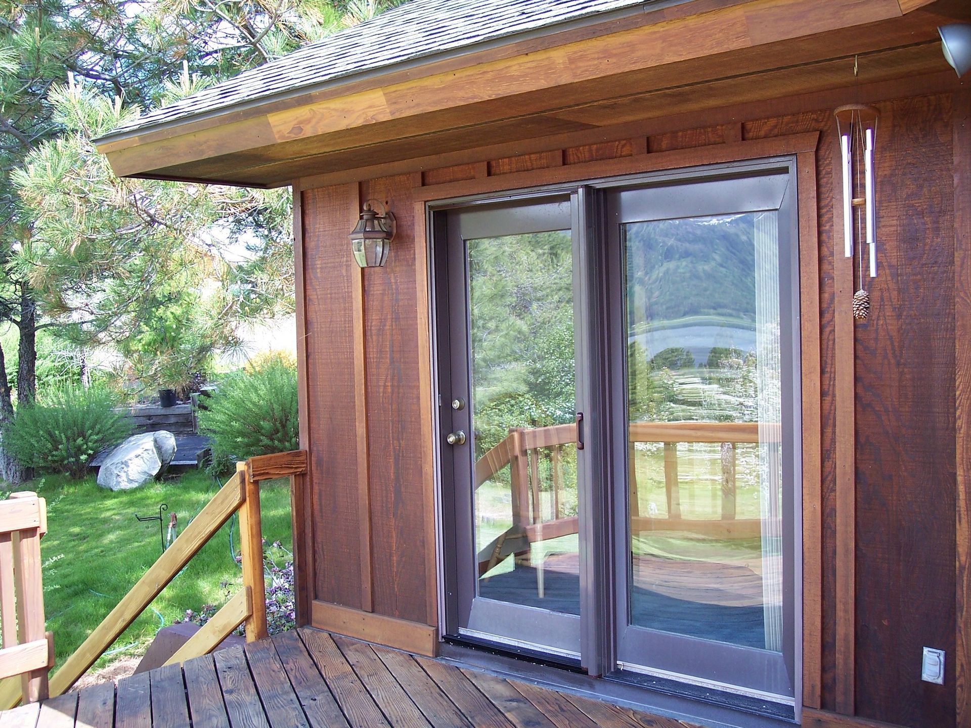 Wooden cabin porch with sliding glass doors and a railing overlooking a green yard