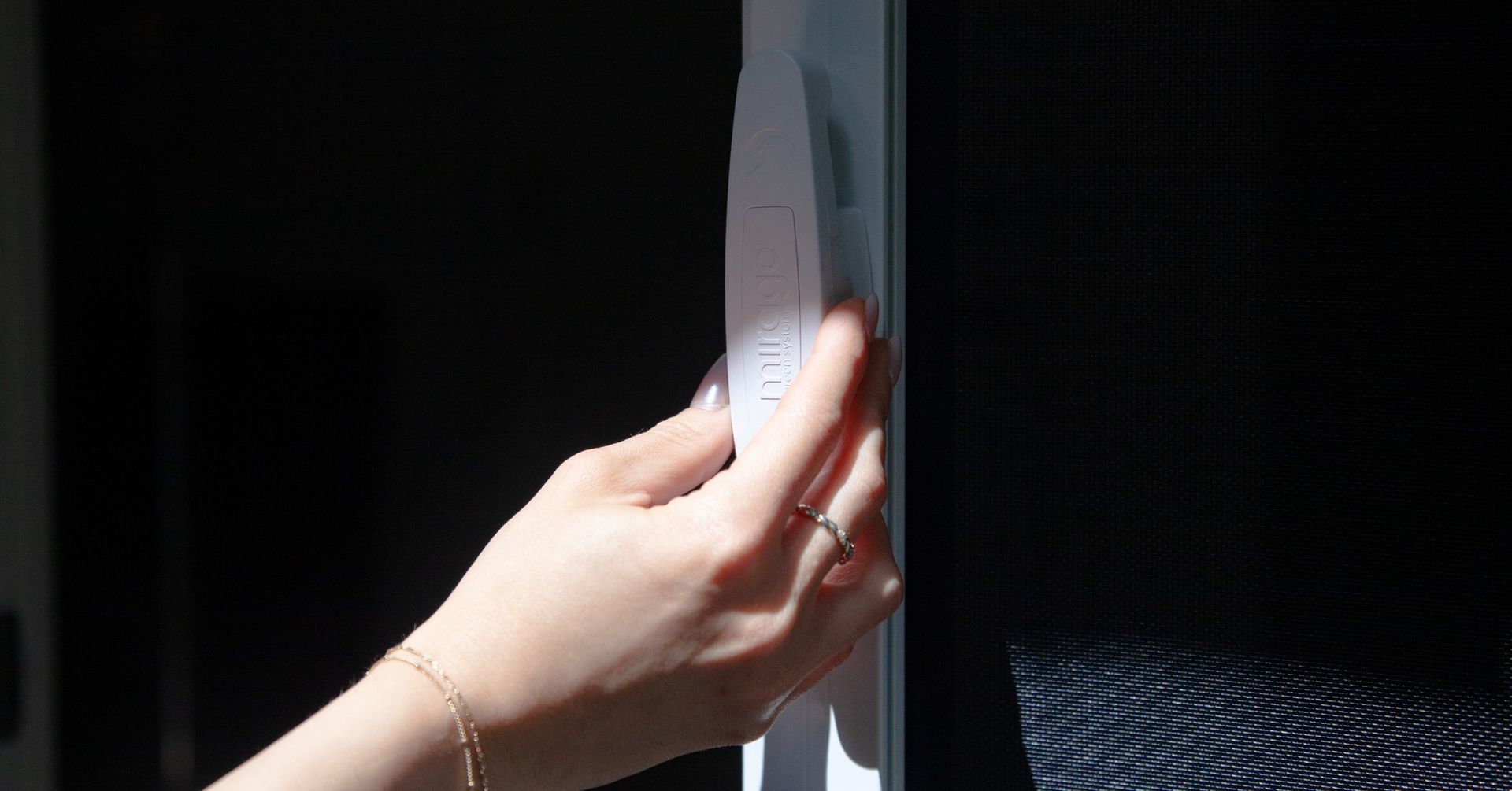 Hand pressing a white wall switch on a dark wall near a black screen.