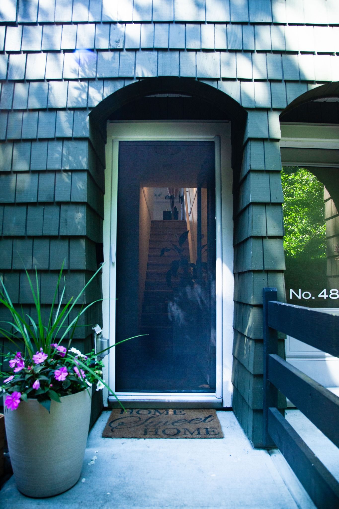 Front door with dark blue siding, potted flowers, and a narrow porch walkway.