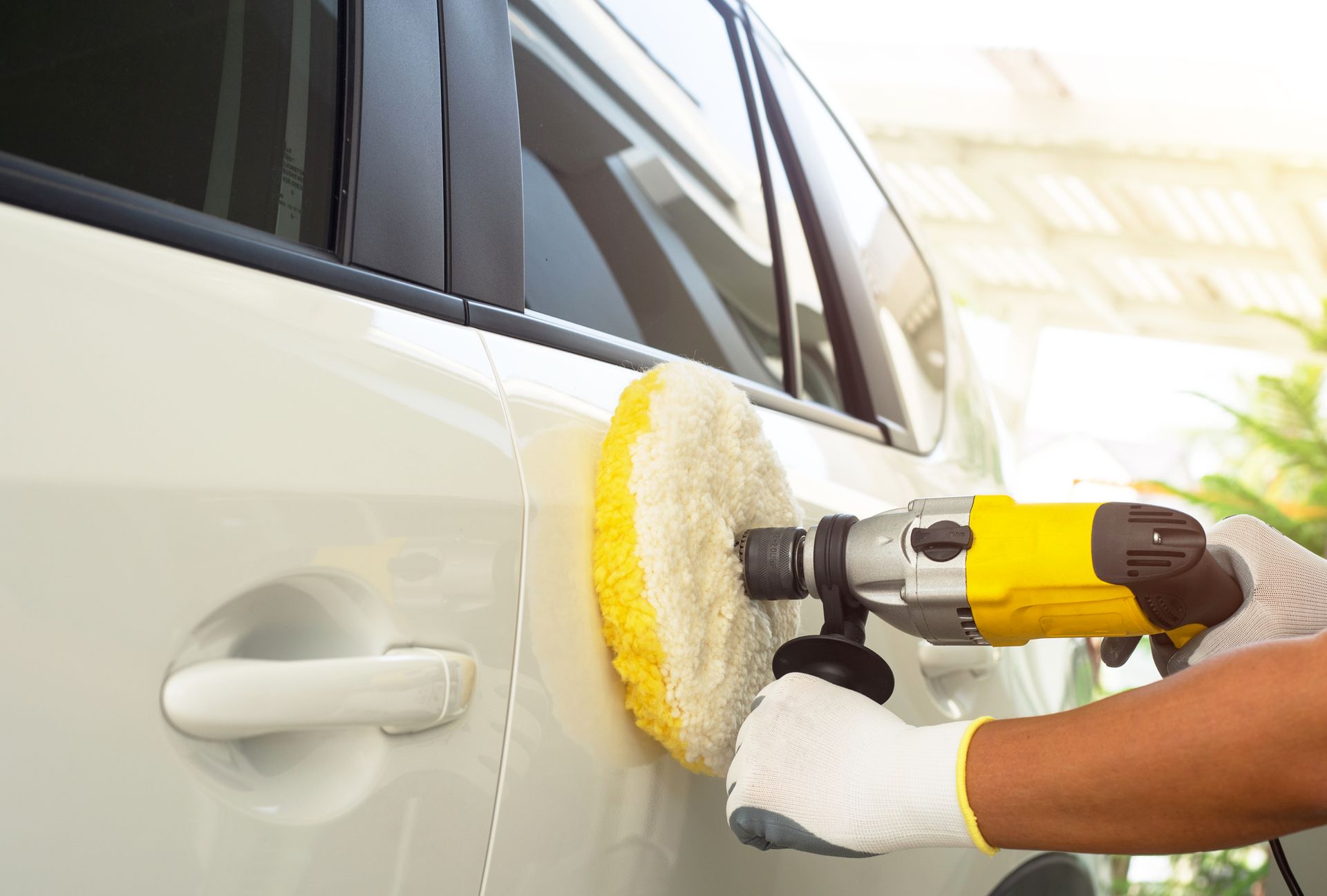 Person polishing a white car door with a yellow and black electric polisher.