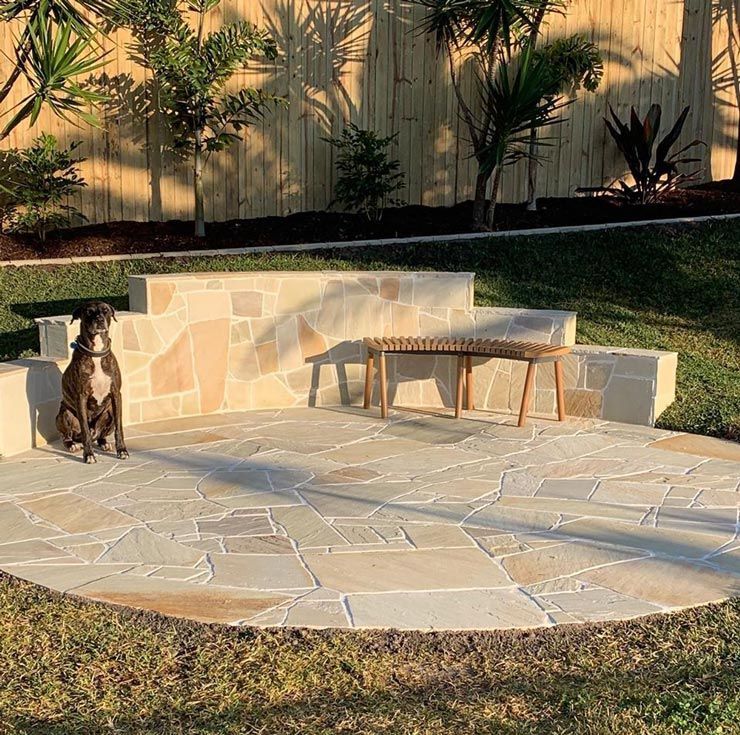 A Dog is Sitting on a Stone Patio Next to a Bench — Caloundra Landscape Supplies in Caloundra, QLD