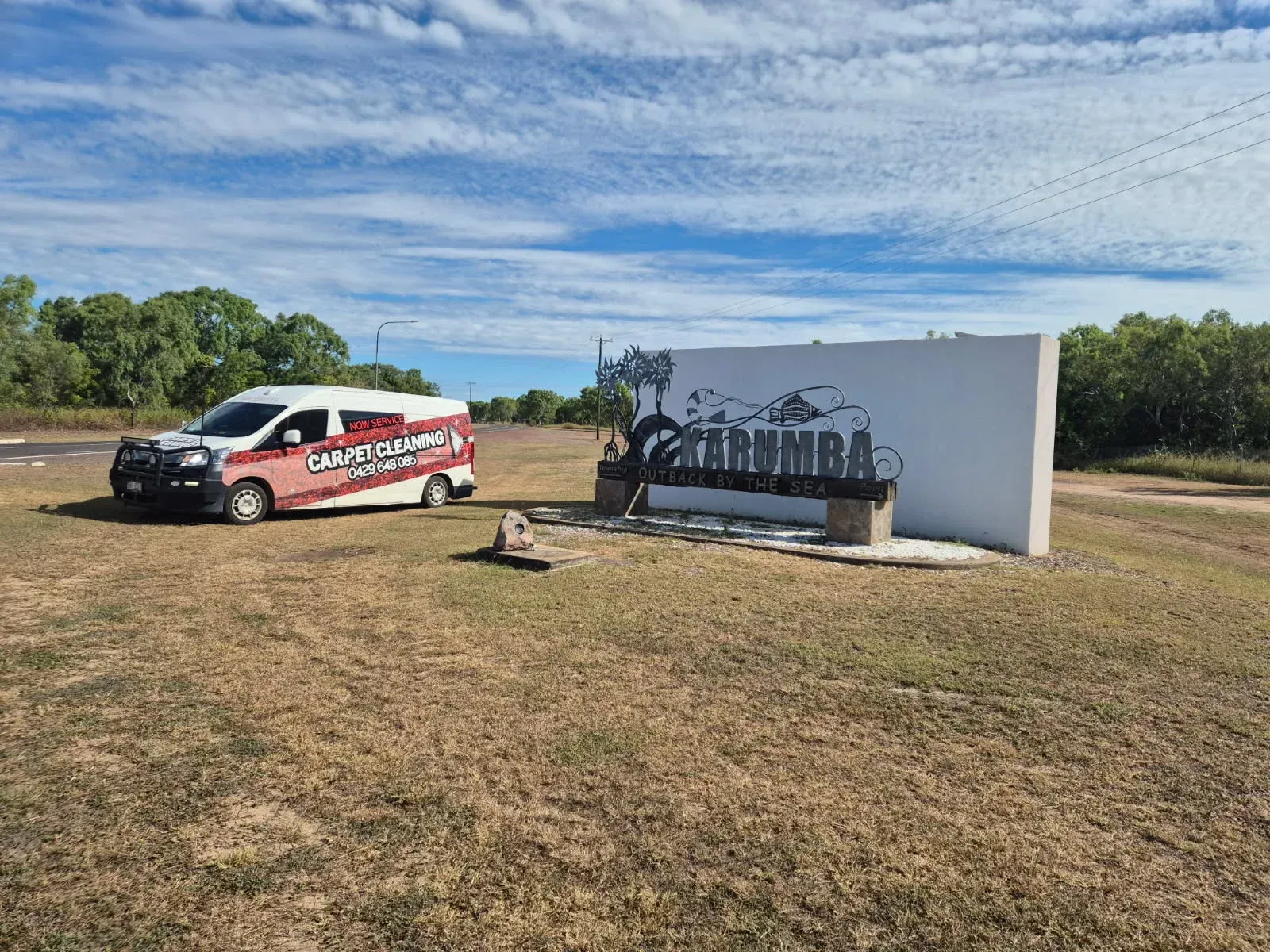 Red and white service truck parked beside a large white sign in a grassy field under a blue sky — NQW Services In Tully, QLD