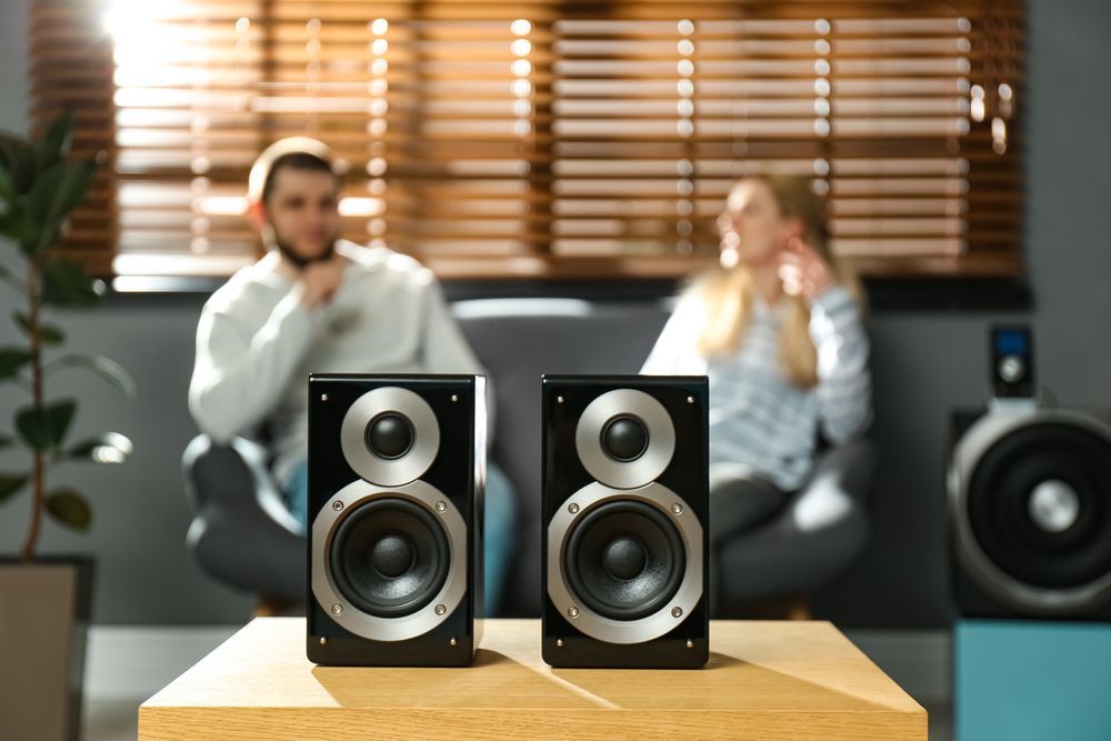A man and a woman are sitting on a couch in front of speakers.