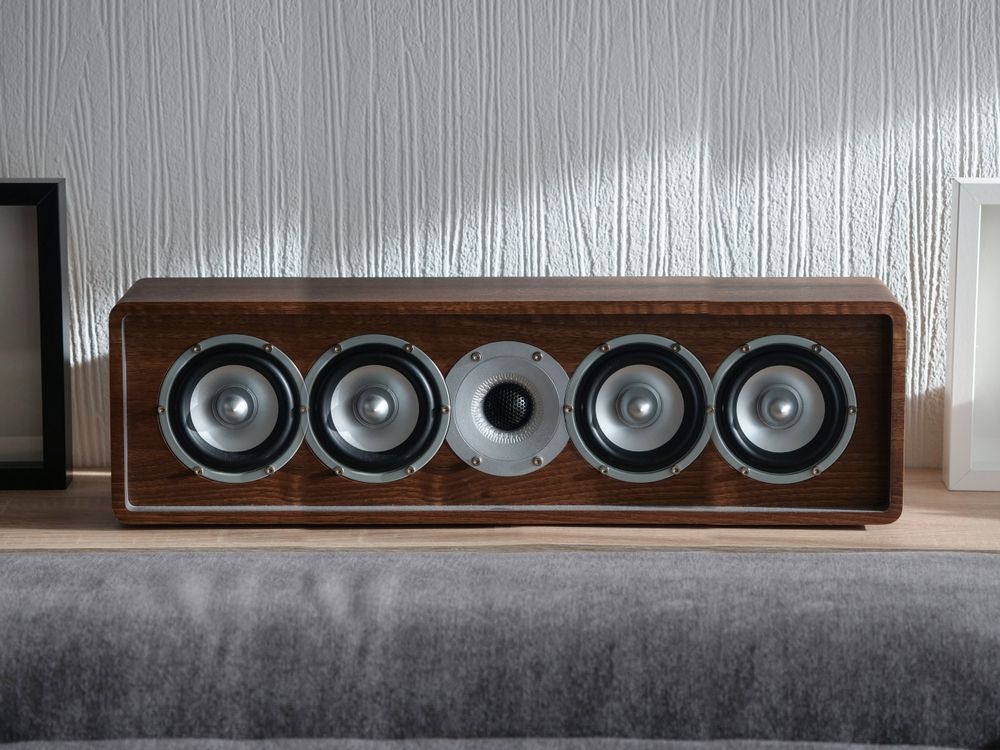 A wooden speaker is sitting on a shelf in a living room.