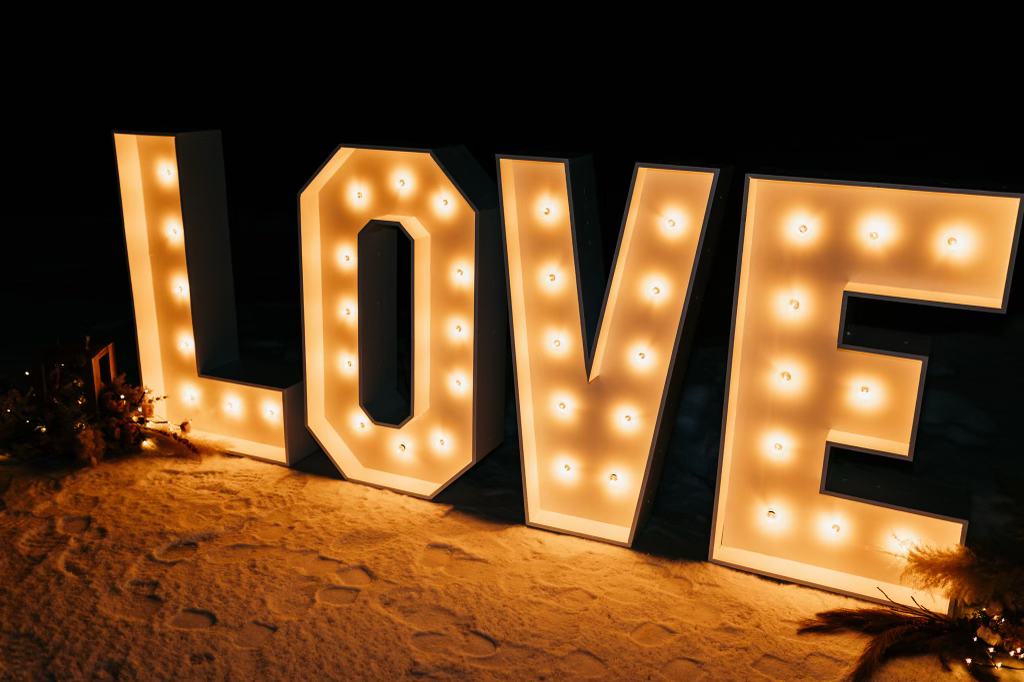 The word love is lit up in large letters on the beach at night.