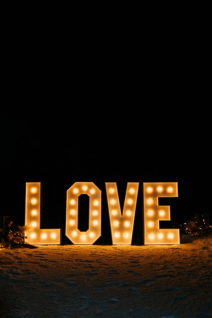 The word love is lit up in large letters on the beach at night.