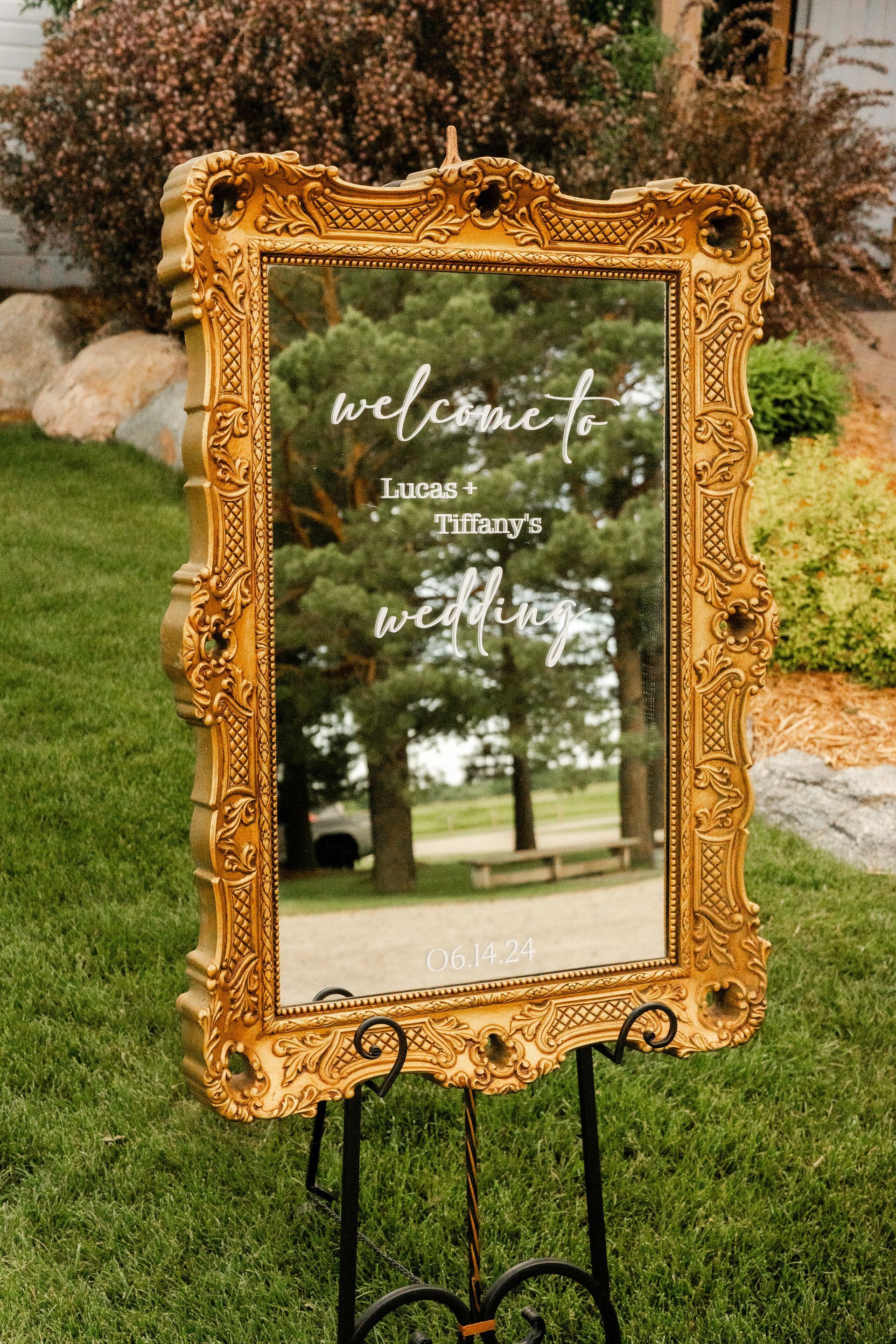 A large gold framed mirror is sitting on top of a metal easel in the grass.