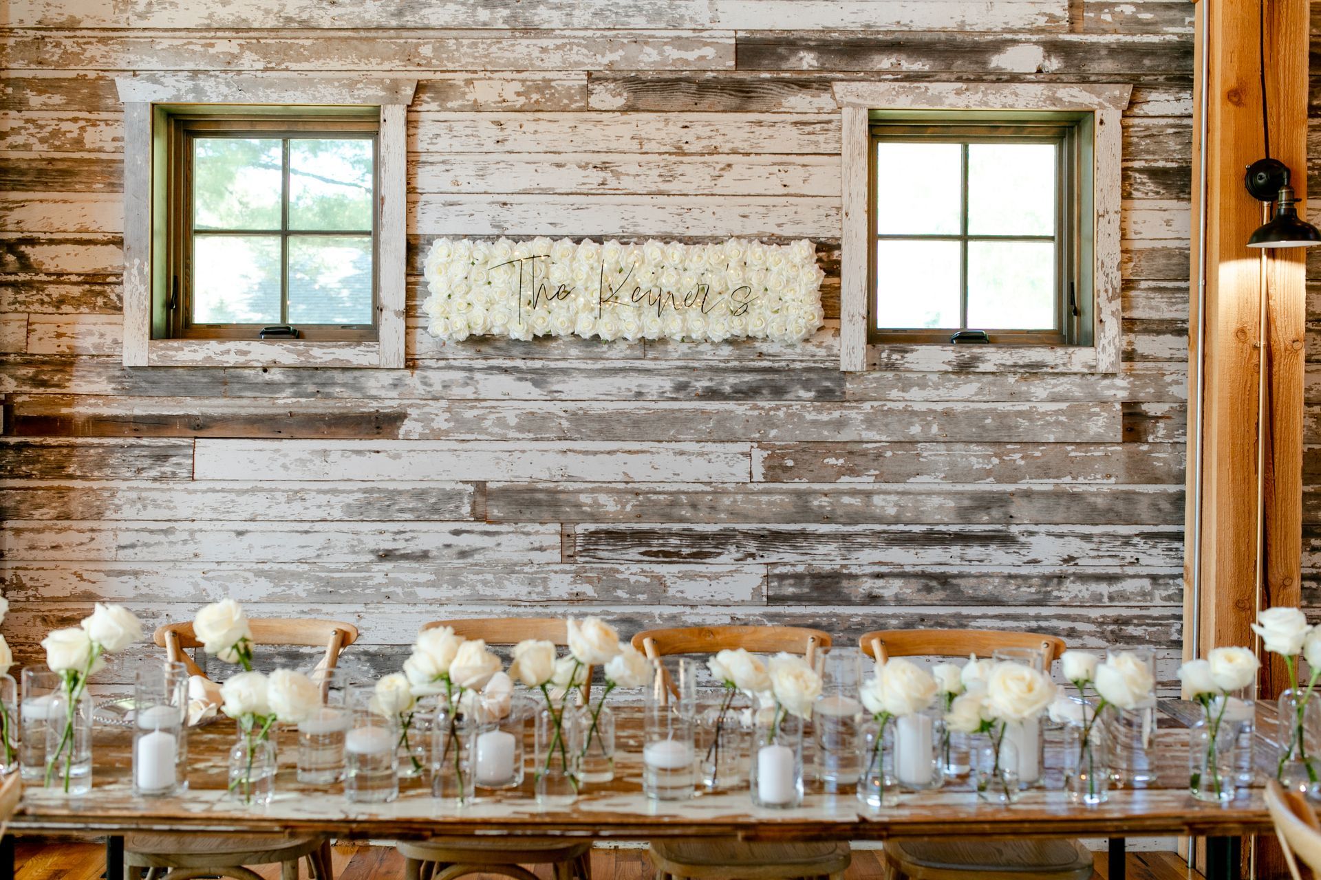 A long table with flowers and candles on it in front of a wooden wall.