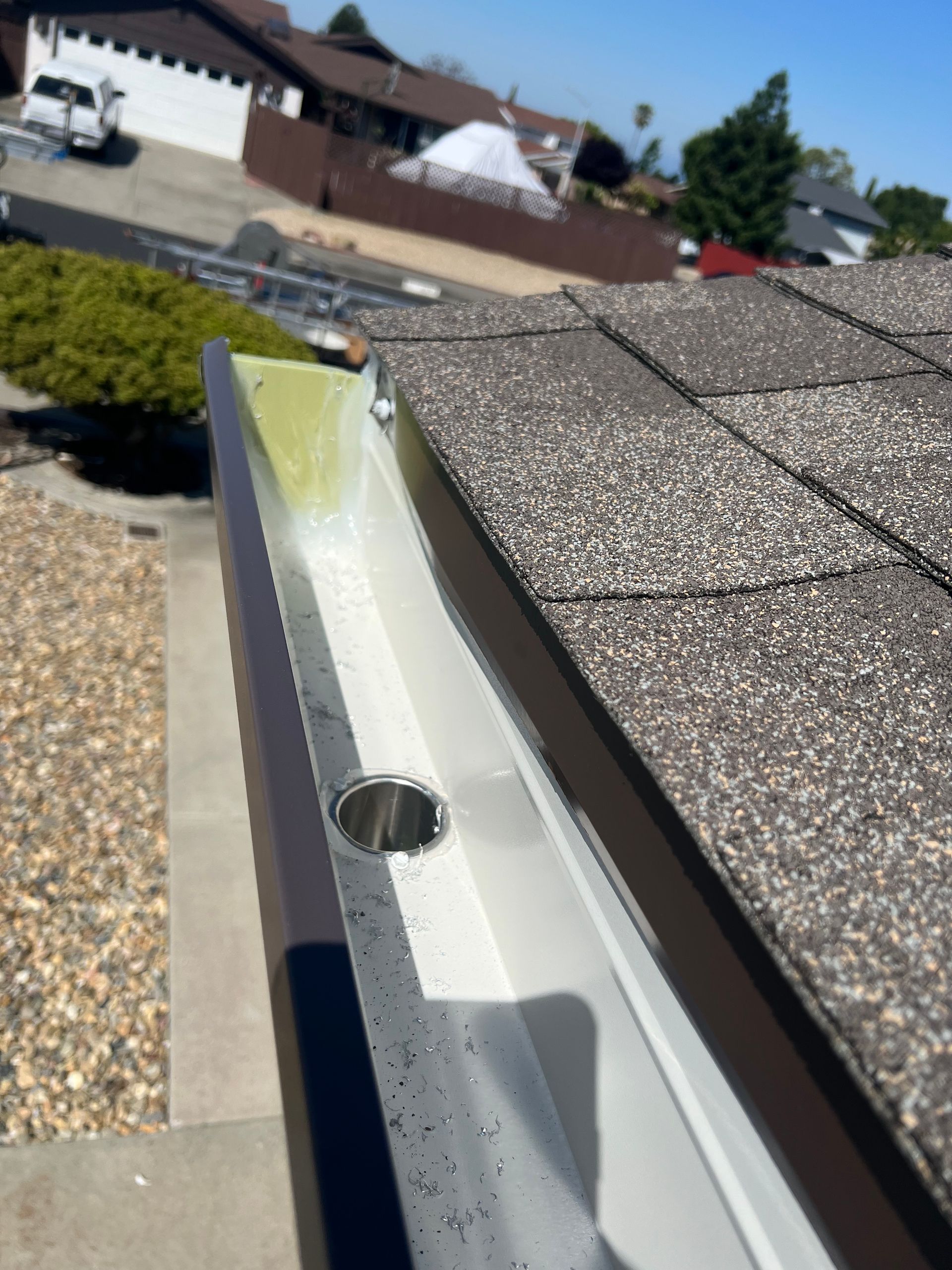 Gutter downspout and corner bracket under a house roofline beside a brick wall
