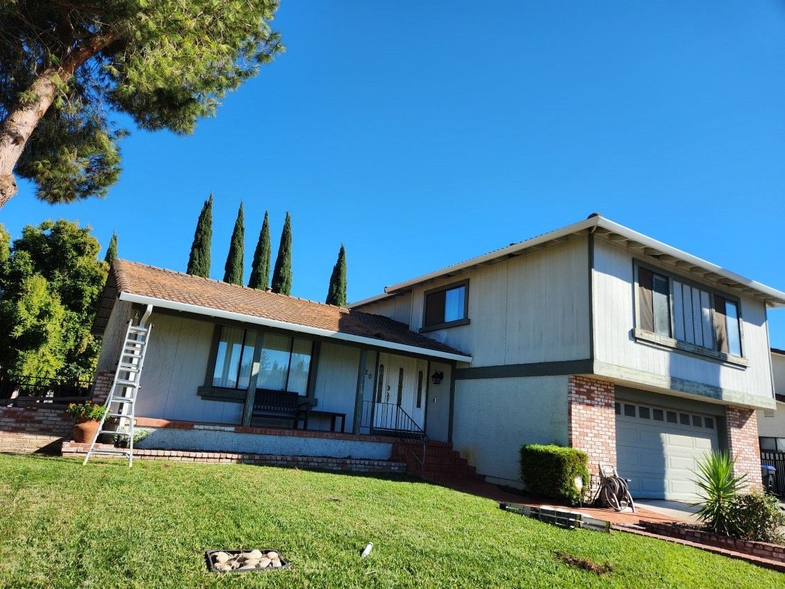 Worker in gray gloves cleaning a black gutter along a house roofline under a blue sky