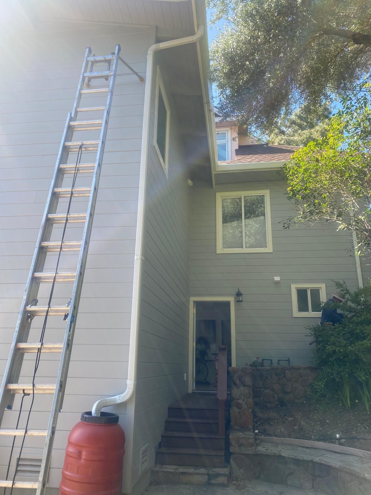 House exterior with a tall ladder leaning to the roof and a red rain barrel by the wall