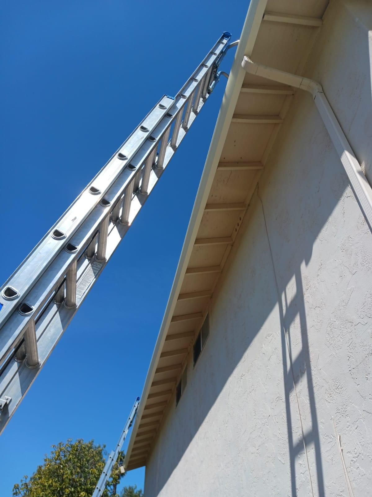 Tall metal ladder leaning against a light-colored building under a clear blue sky