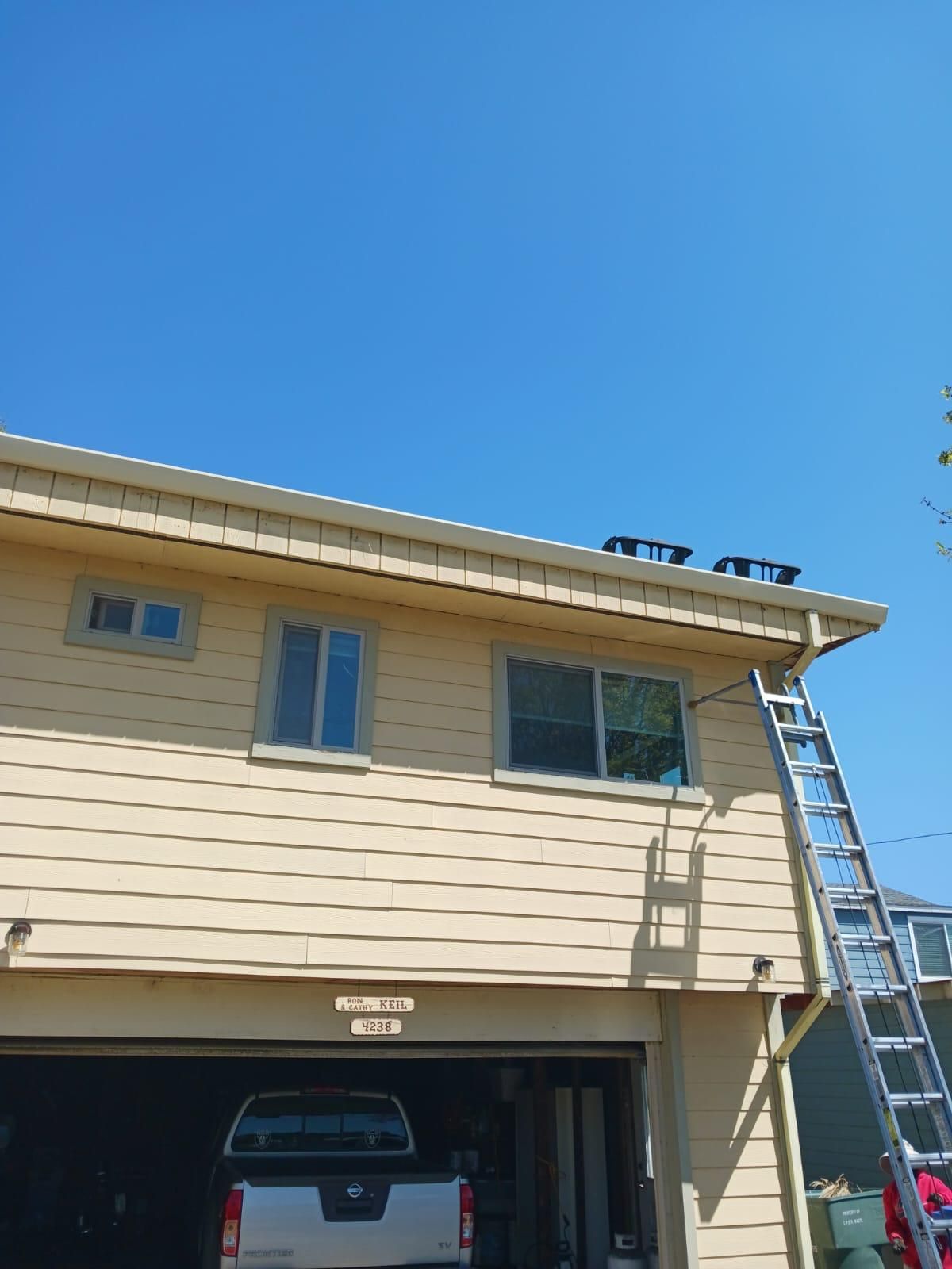 Two-story beige house with ladder on the right and blue sky overhead