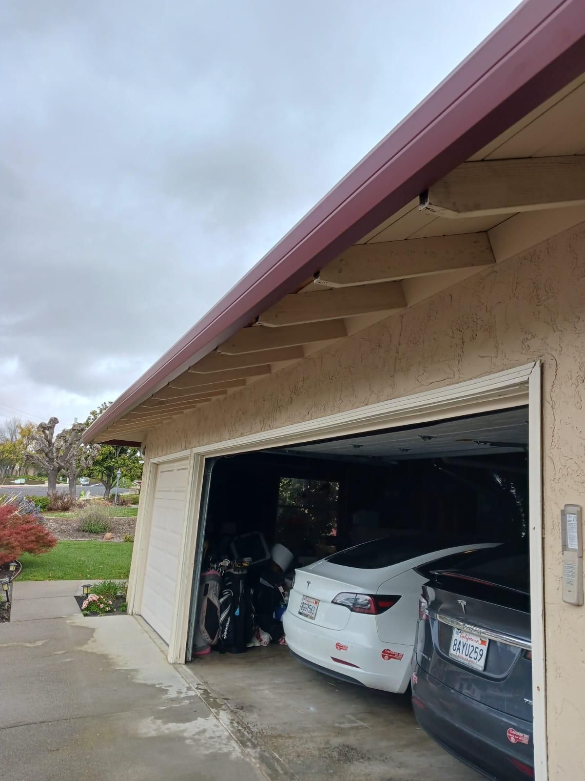 Open garage with two parked cars under a beige house roof on a cloudy day