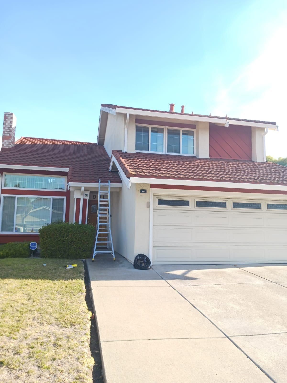 Suburban two-story house with red roof, white garage, and ladder leaning against the front exterior