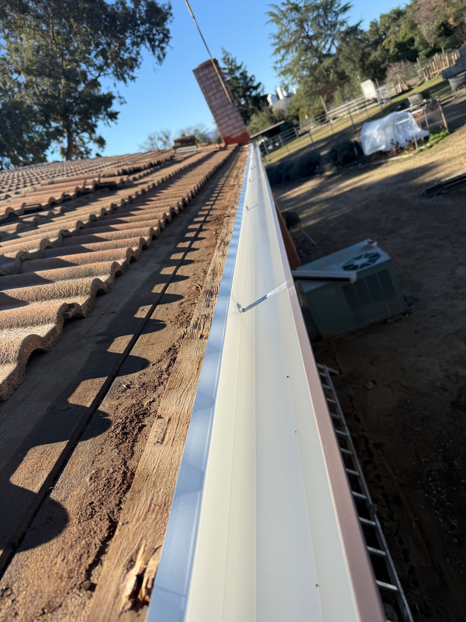 Person using a cordless drill to repair an exterior roof eave above a house window