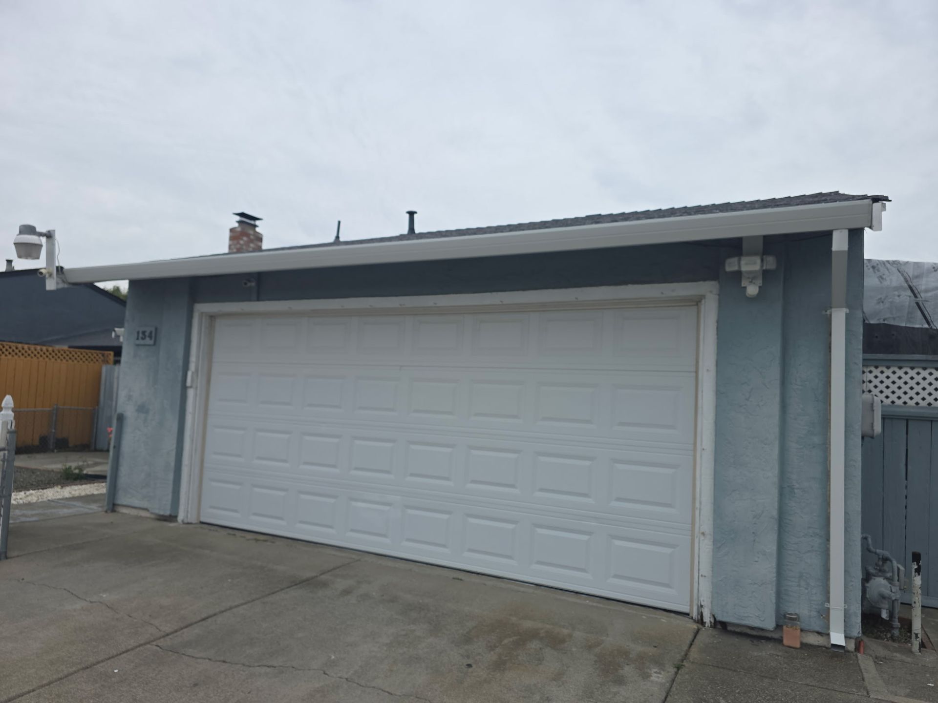 White garage door on a gray building beside a concrete driveway under an overcast sky