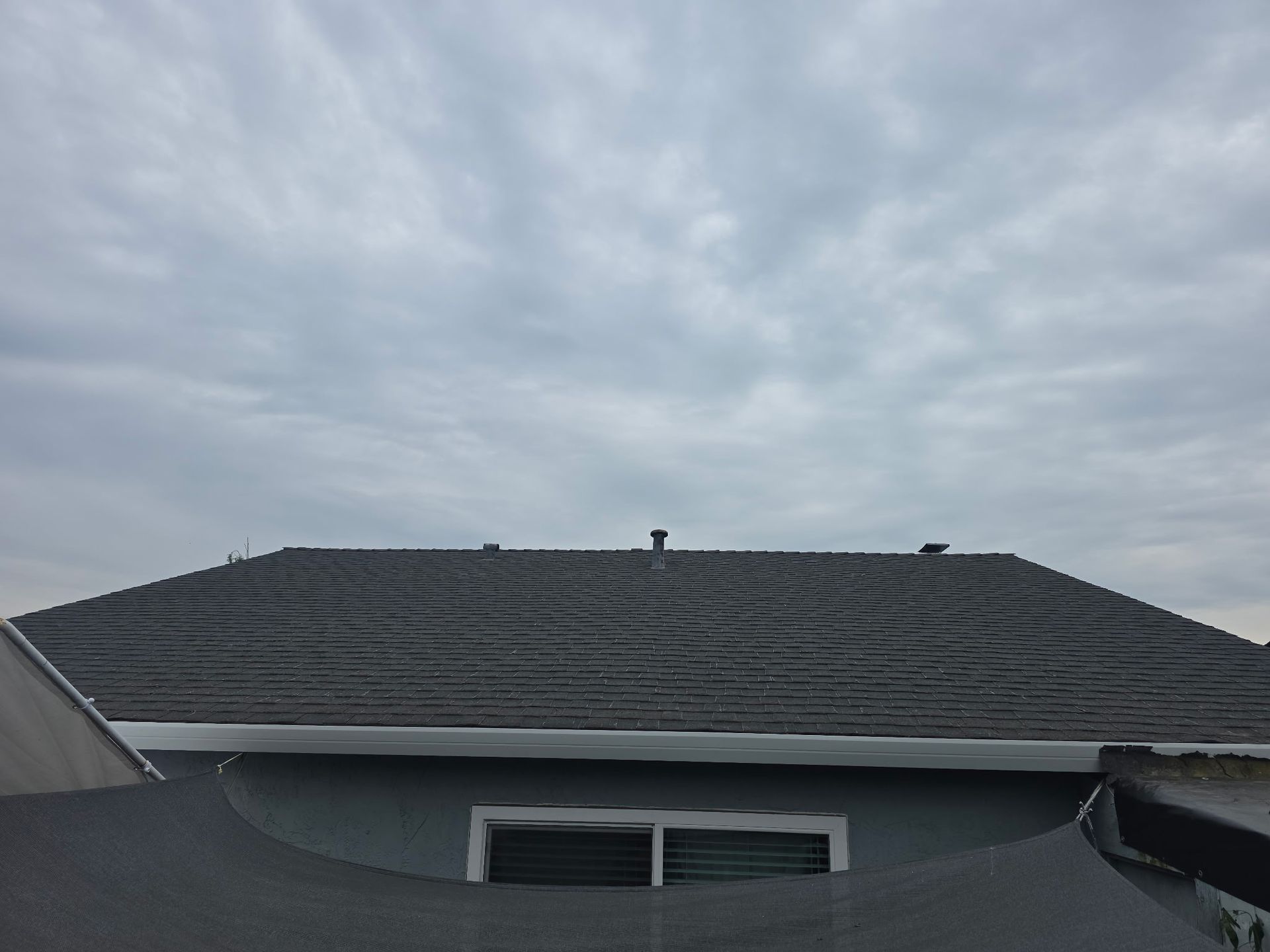 Dark gray roof under a cloudy sky, with a house window below the eaves.