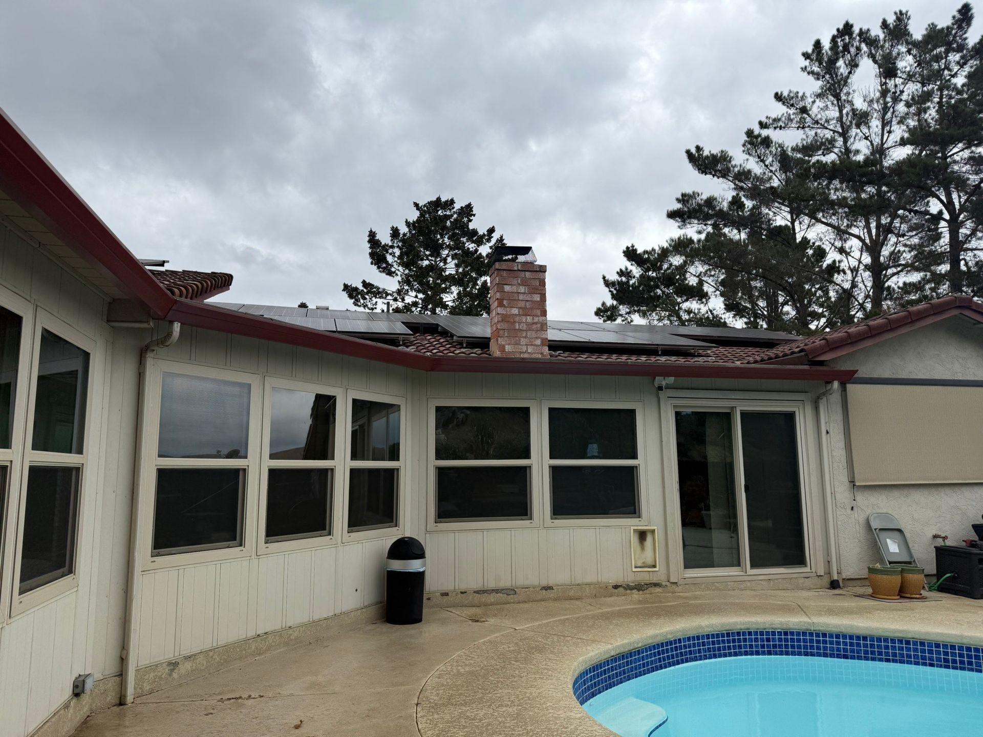 Back patio with white house exterior, windows, grill, and a small blue pool under cloudy sky