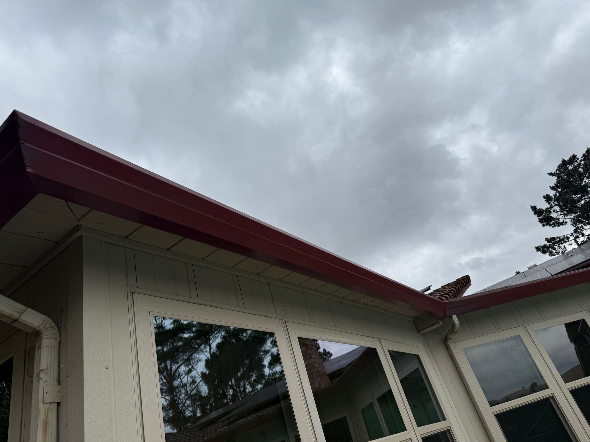 Exterior of a house with white walls, red roof trim, and cloudy gray sky above