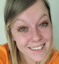 Smiling person in an orange hoodie taking a close-up selfie indoors