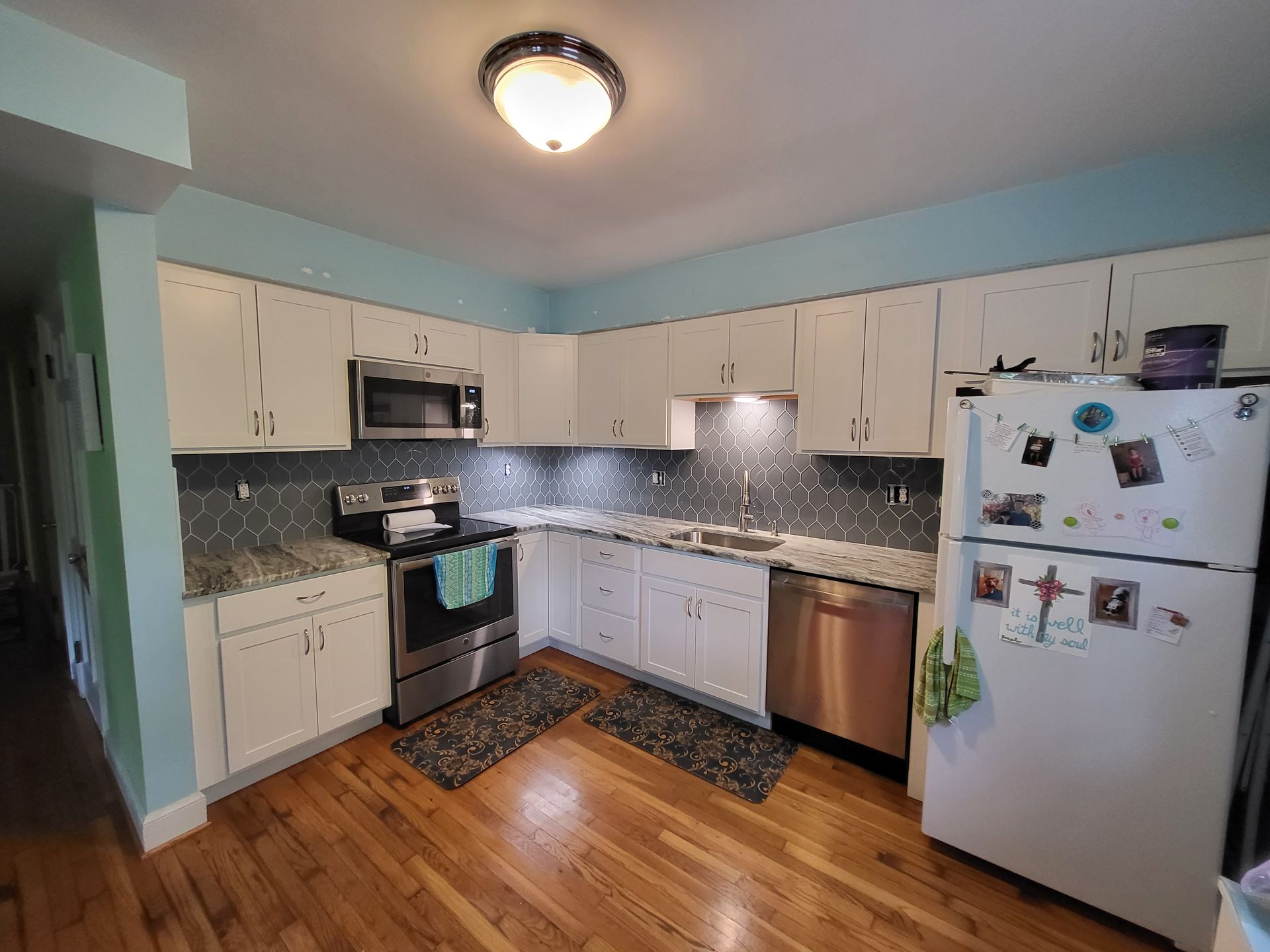 Bright kitchen with white cabinets, speckled countertops, stainless appliances, and wood floors