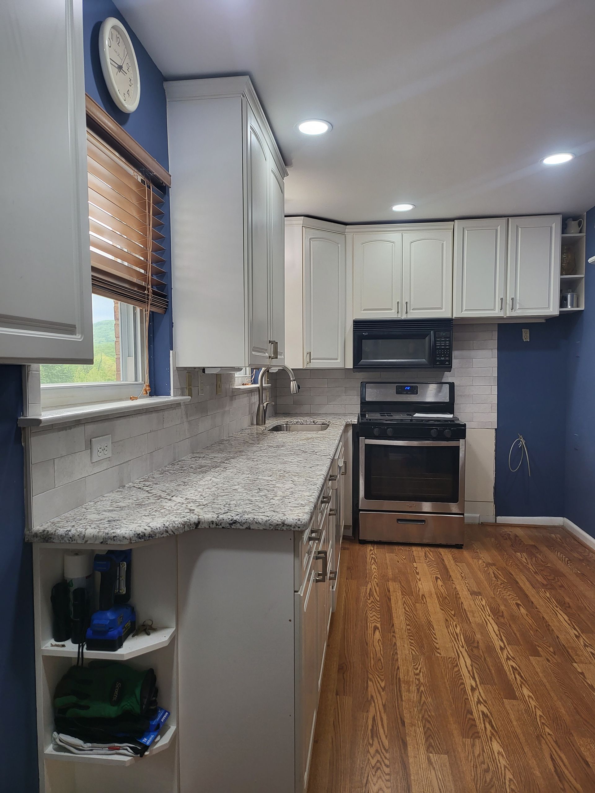 Bright kitchen with granite counters, white cabinets, stainless stove, and blue accent wall.