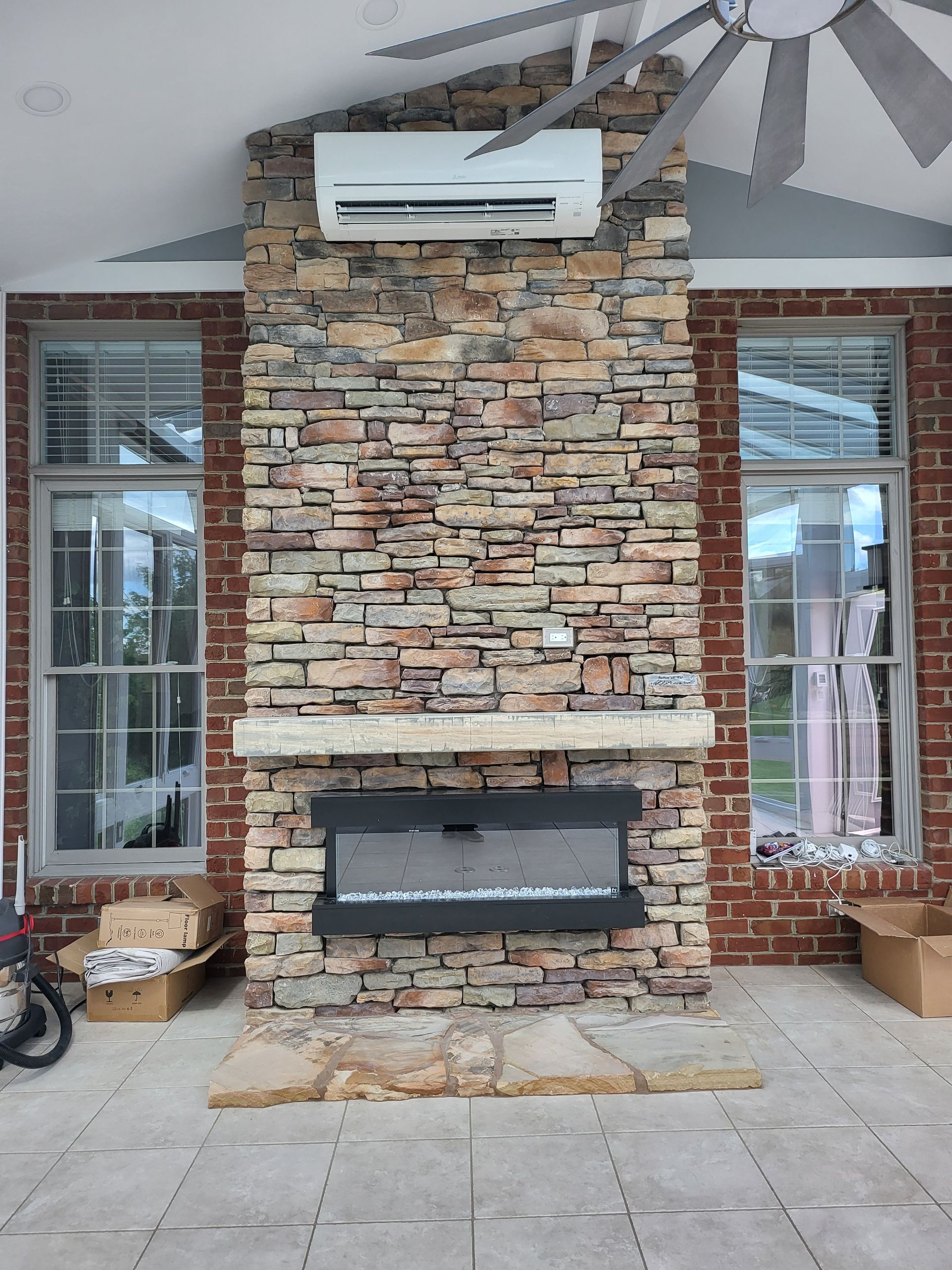 Stone outdoor fireplace under a covered patio with white windows and gray tile flooring