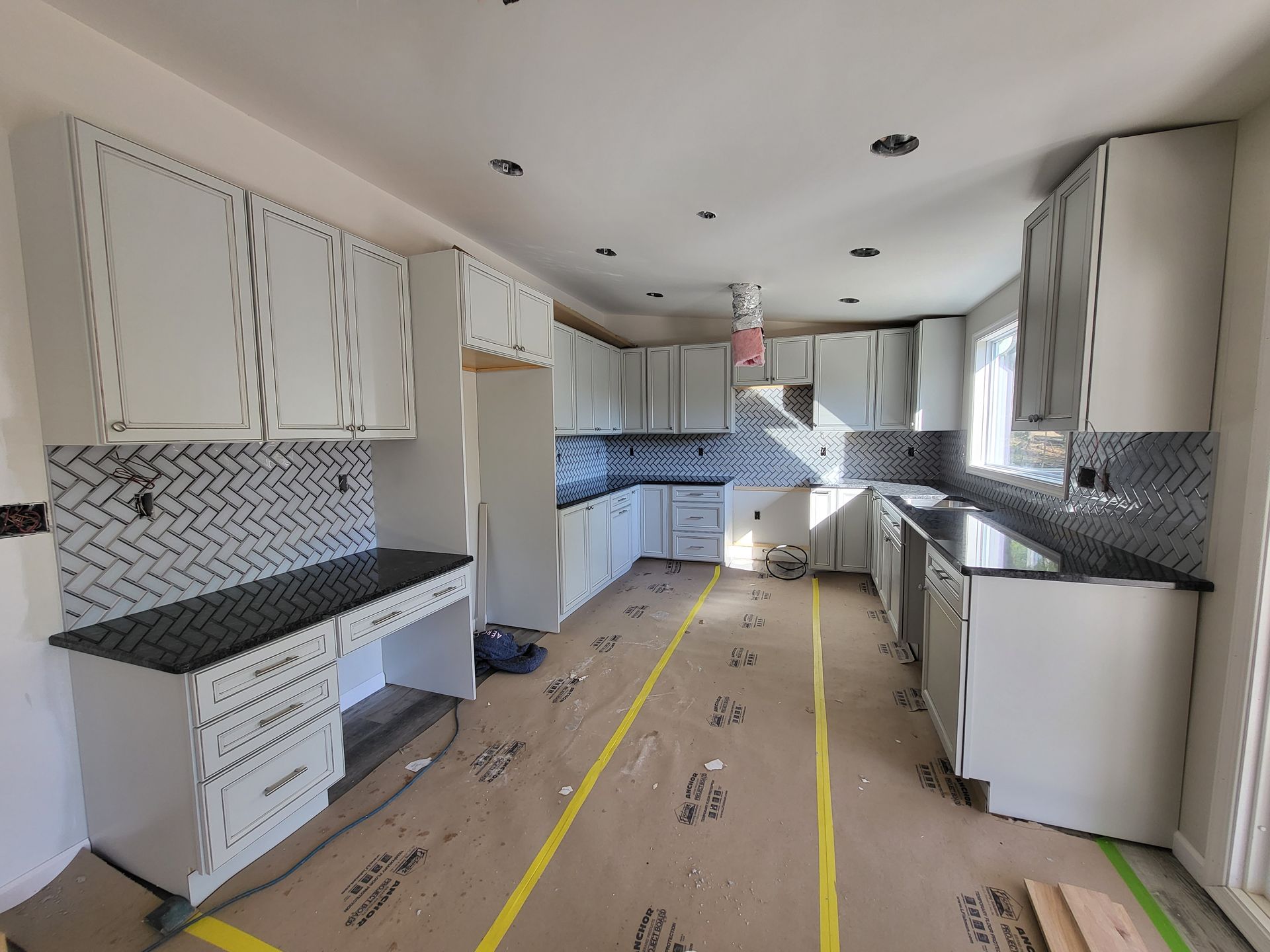 Renovated kitchen with white cabinets, dark countertops, and covered floor in progress