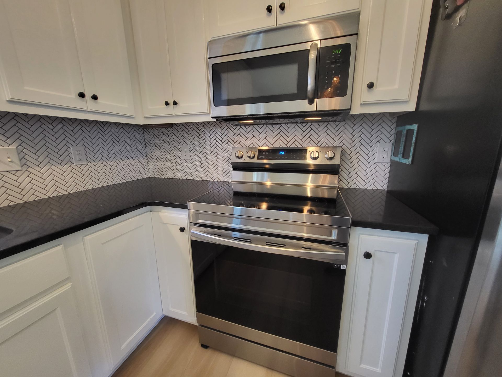 Modern kitchen with white cabinets, black countertops, stainless steel microwave and stove, and herringbone backsplash