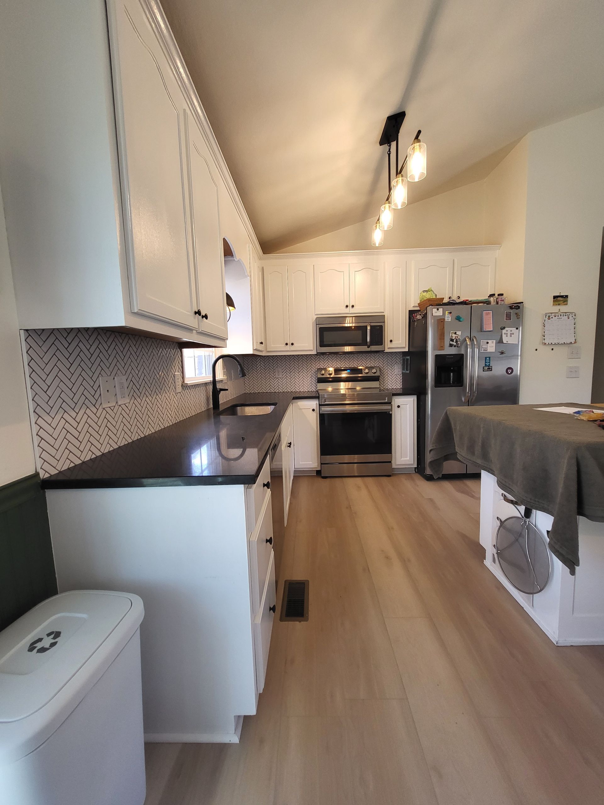 Narrow modern kitchen with white cabinets, wood floor, stainless stove, and a dining table at right.