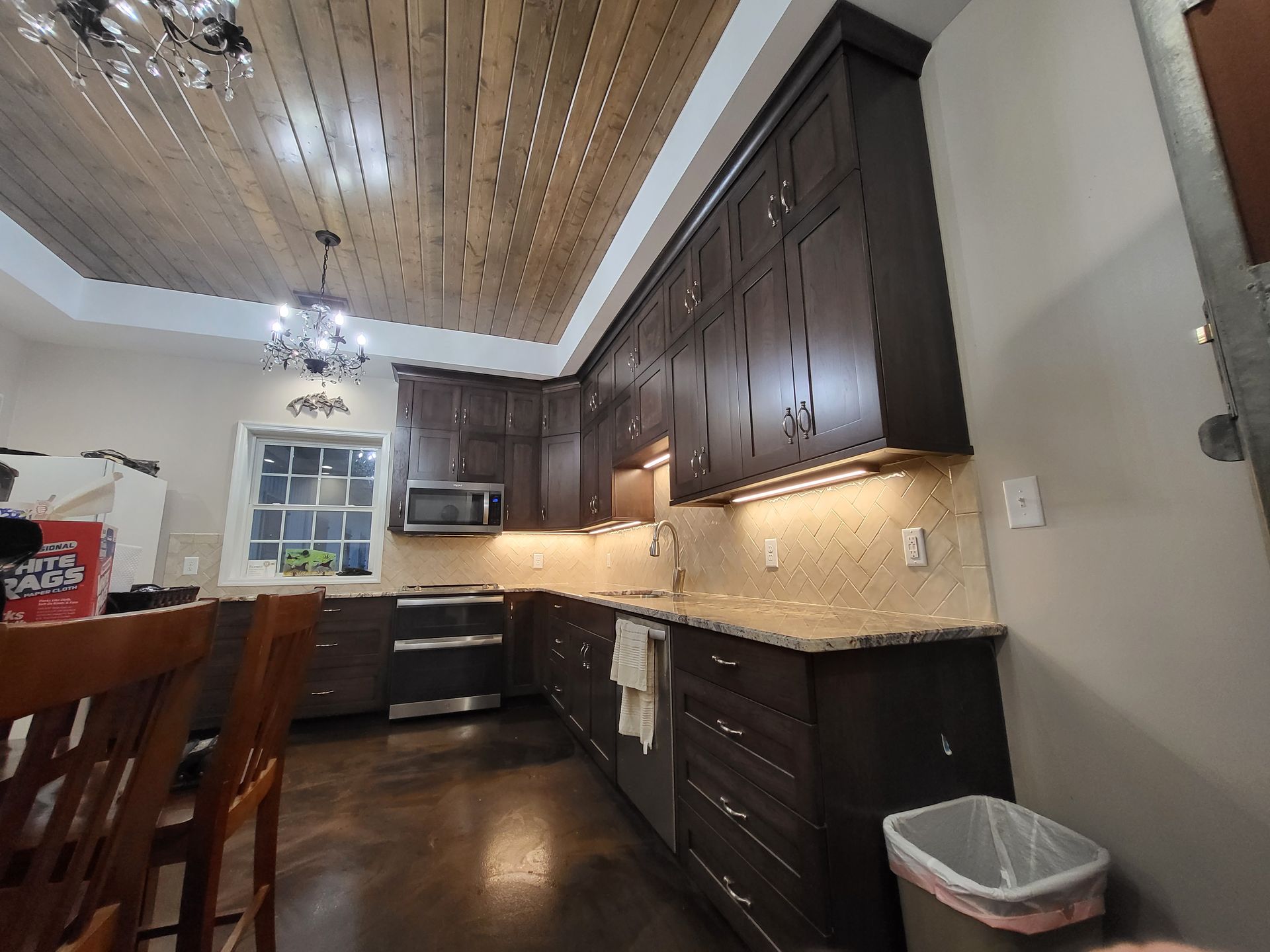 Modern kitchen with dark wood cabinets, stone counters, wood ceiling, and a dining table in the foreground