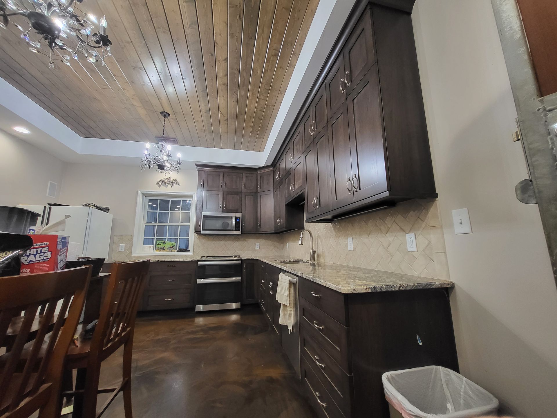 Modern kitchen with dark wood cabinets, granite counters, stainless appliances, and wood plank ceiling